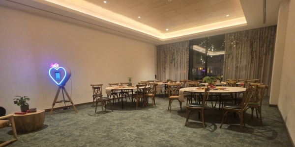 a large room with 4 round tables and chairs set up for a dinner, and floor to ceiling window at one end of the room