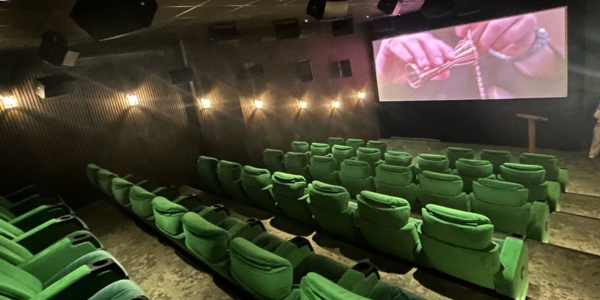 a warmly lit auditorium with rows of comfortable green seats facing a projector/cinema screen