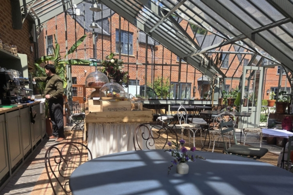 the inside of a greenhouse restaurant, with a coffee bar, tables and chairs