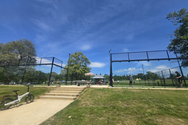 two padel courts with a shaded area between them, and an e-bike parked in front