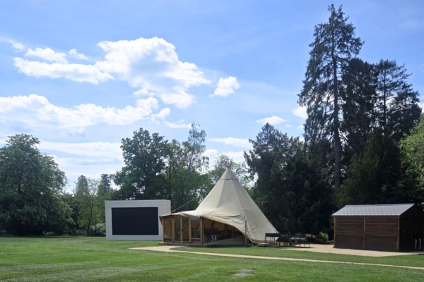 a tipi in the middle of a grassy field with a giant outdoor screen to one side