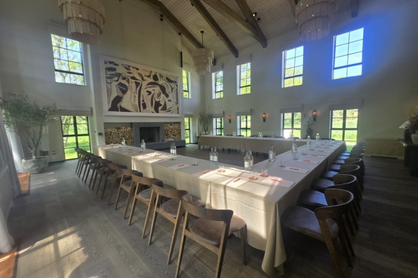 a large room with lots of windows and natural light. Tables and chairs are set up for a meeting in a horseshoe layout out, in front of a large fireplace, and a tapestry hangs above the fireplace.